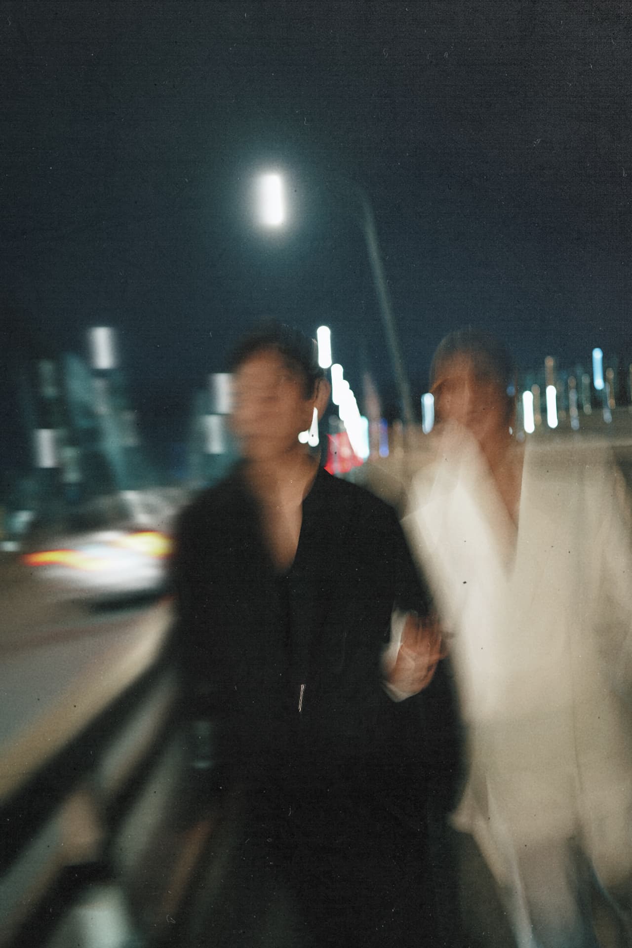 The couple walking along a city bridge at night